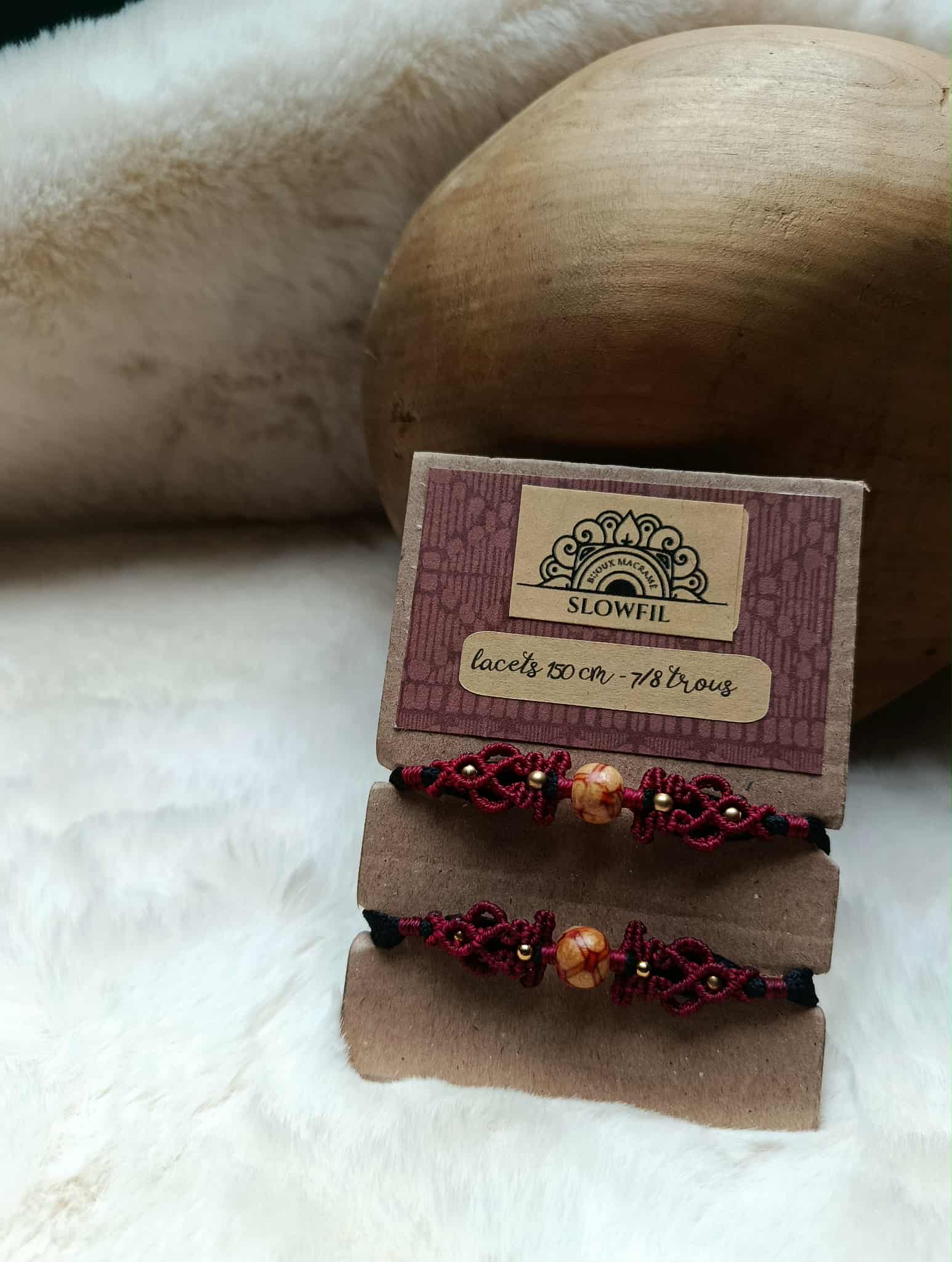 bijou en micromacramé de fil bordeaux tissé autour d'une perle en bois a motif végétal et perle inoxydable en laiton